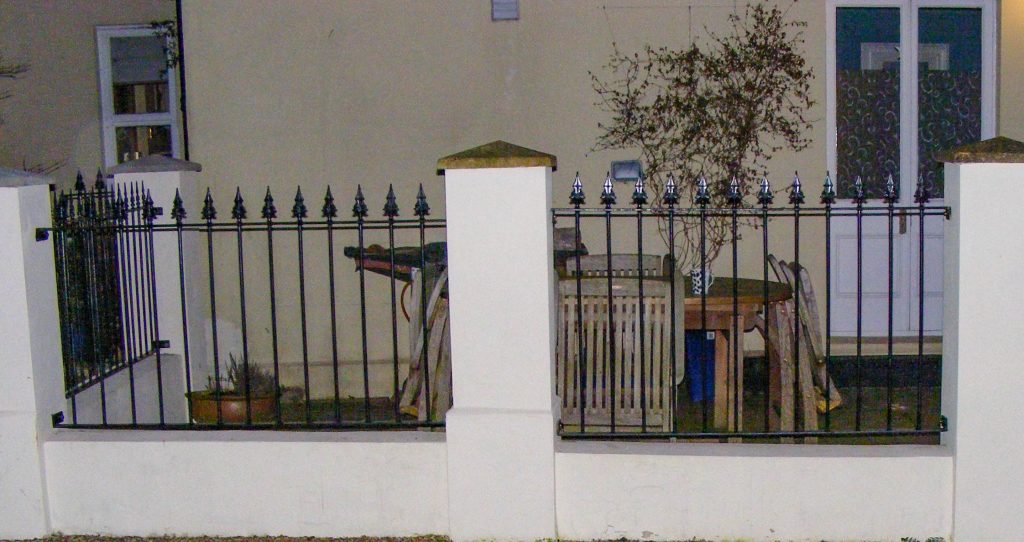 Tall wrought iron railings on a low wall between brick piers