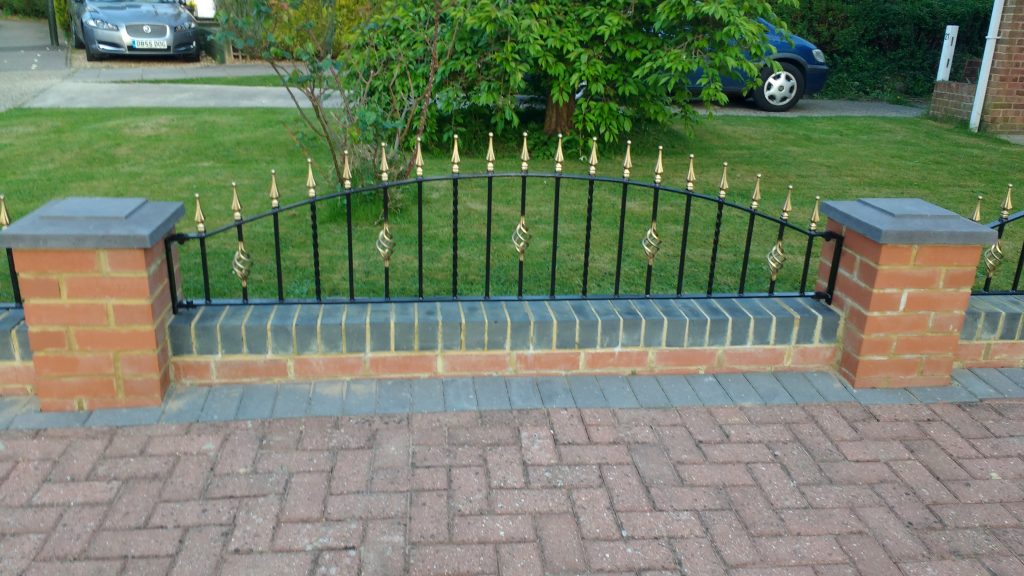 decorative wrought iron railing on a low garden wall with gold painted railing heads